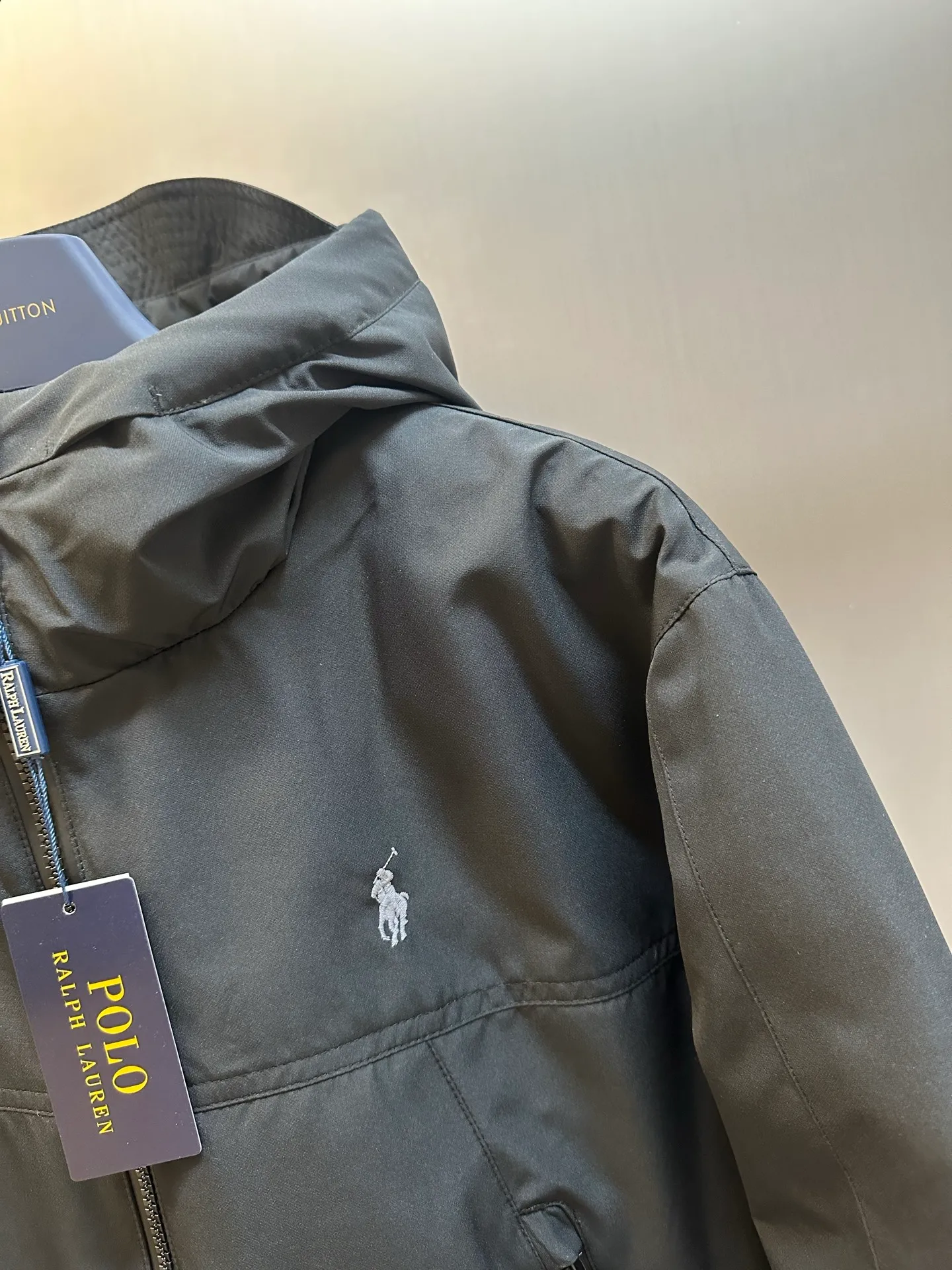 P970 Ralph Lauren logo hooded down jacket. The density of high-density nylon taffeta is about 210T-300T. The surface is smooth and slightly matte. It has excellent windproof and waterproof performance (with DWR water-repellent treatment). It has strong wrinkle resistance and is easy to care for. It is in line with the positioning of American casual "durable and practical".  The inner lining is made of 100% polyamide. The high-density and tight weaving process prevents fine lint from getting out of the gaps in the fabric. The smooth surface improves the putting on and taking off experience, and the excellent wear and tear resistance ensures damage caused by frequent use, while the light and soft texture does not affect the overall weight.  It uses 90 white duck down with a weight of 220g to ensure excellent thermal insulation performance. After strict screening and processing, the velvet is not easily drilled, ensuring durability. The classic jacket has a slightly loose fit, with slightly dropped shoulder lines (the shoulder width is 1-2cm wider than the standard fit). The length reaches the hips, and the sleeves are slightly tapered straight sleeves, taking into account freedom of movement and casual style.  The adjustable Velcro on the cuffs allows you to freely adjust the tightness according to the thickness of your wrist and personal preferences, effectively preventing cold wind from intruding, and improving the warmth performance. Two zippered pockets on the front are convenient for placing frequently used items, and the zipper design ensures that items are not easily lost. A built-in pocket on the left side of the chest provides a safe storage space for some small private items.  The drawstring design at the hem allows you to adjust the shape of the jacket according to your body shape and dressing needs. Whether it is loose and casual or slim and neat, you can easily control it.  Polo horse logo on the left chest: flat satin stitch embroidery (satin embroidery), using 100% polyester high color fastness embroidery thread (the color number is consistent with the brand's standard red color card), the stitch density is 12-15 stitches/cm, the outline of the horse logo is clear, and the details of the rider and horse are burr-free. Precise positioning through the template (12cm from the bottom of the collar and 8cm from the placket) ensures symmetry and centering.  size：s m l xl